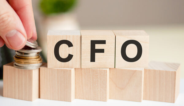 The word CFO written on wood cubes. A man's hand places the coins on the surface of the cube. Business and finance concept. CFO short for Chief Financial Officer